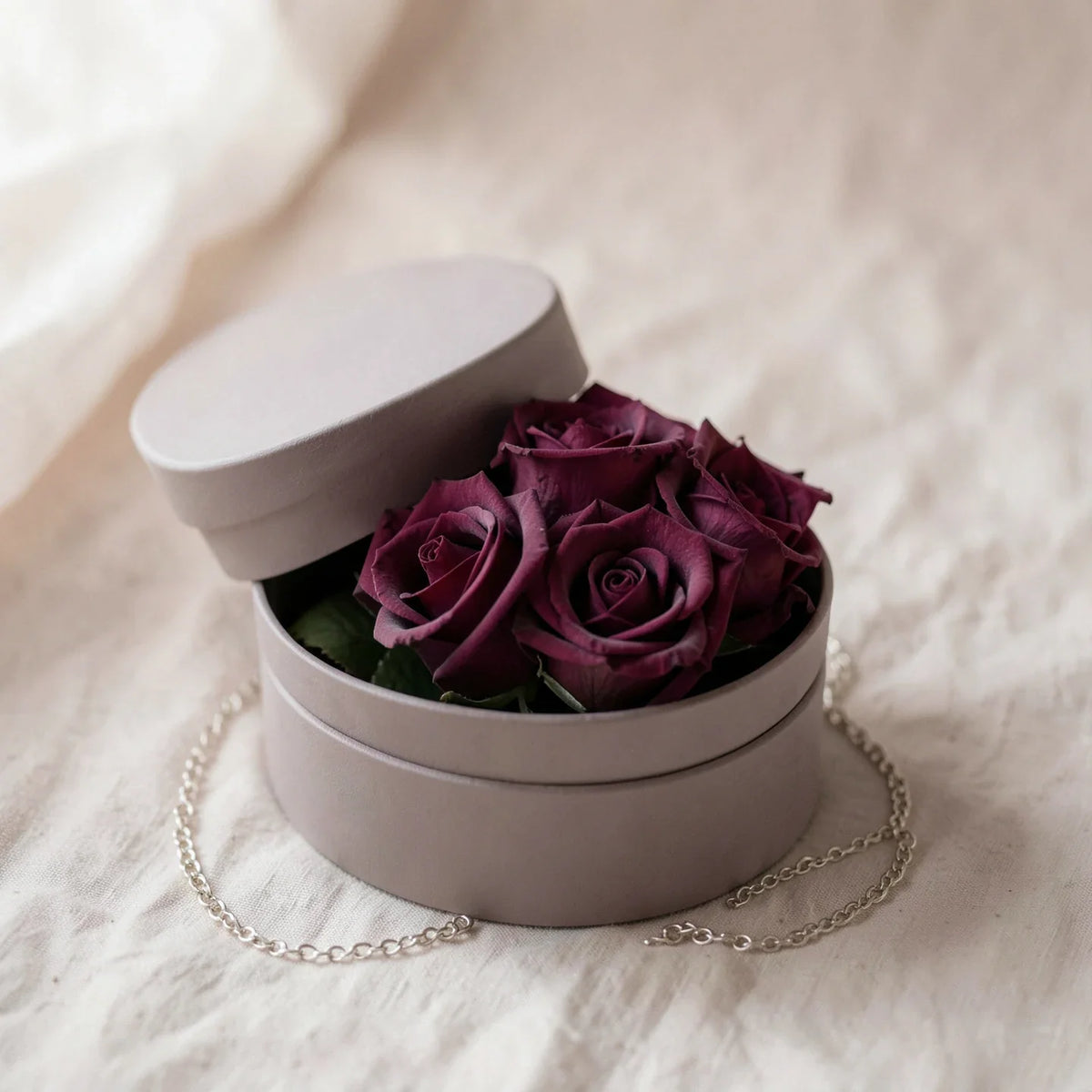 A preserved rose arrangement in a keepsake box with a bracelet beside it