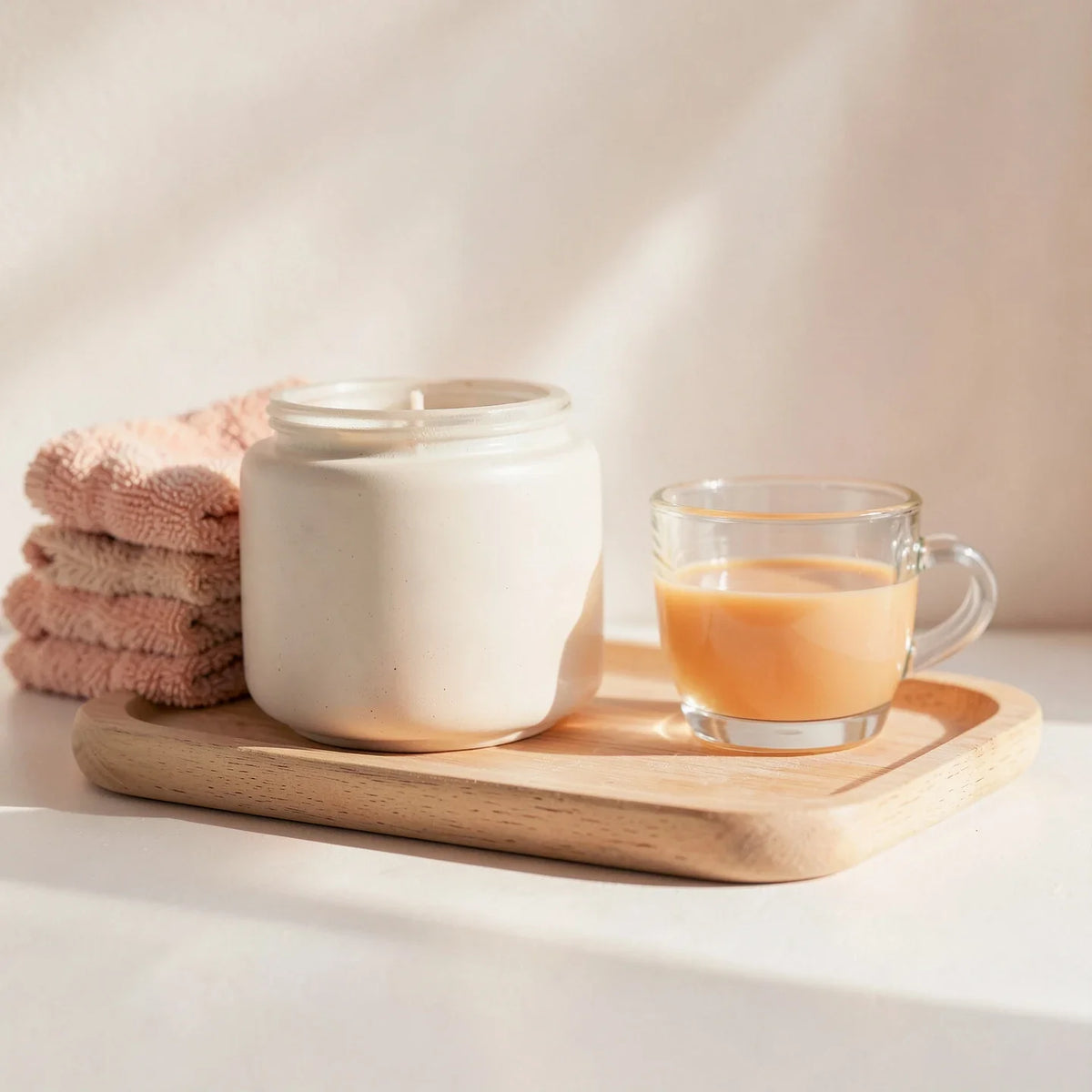 A jar candle, folded towels and a teacup on a wooden tray