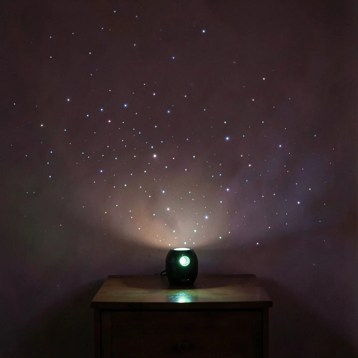 A star projector casting points of light across a dark bedroom wall