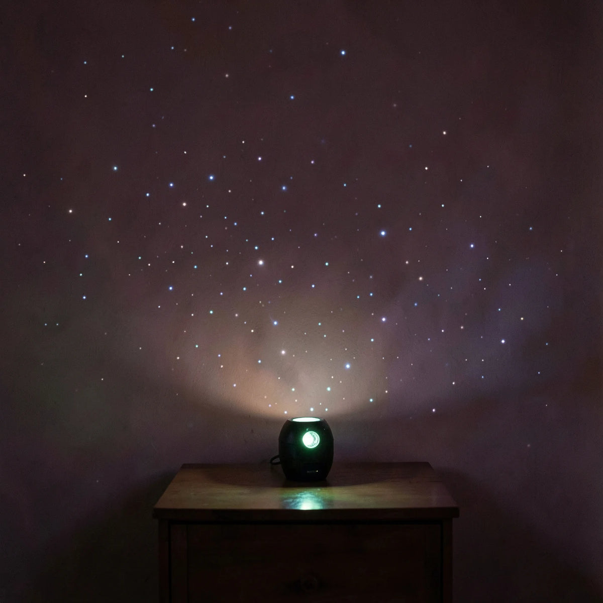 A star projector casting points of light across a dark bedroom wall